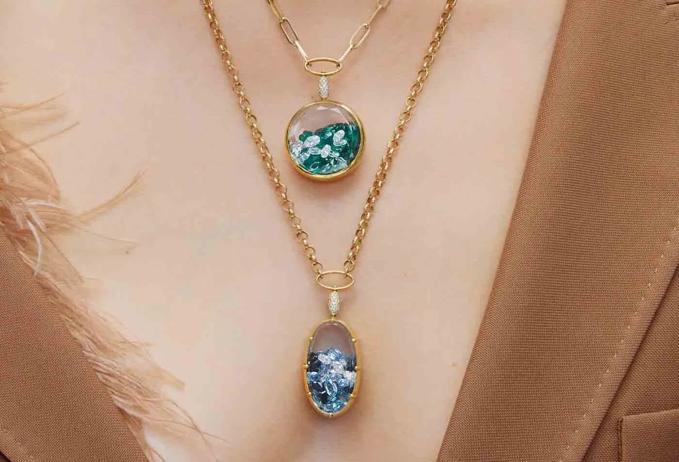 <p>A model wears locket-style pendants from the Aponine Sparks collection with loose gemstones in shades of green and blue</p>
