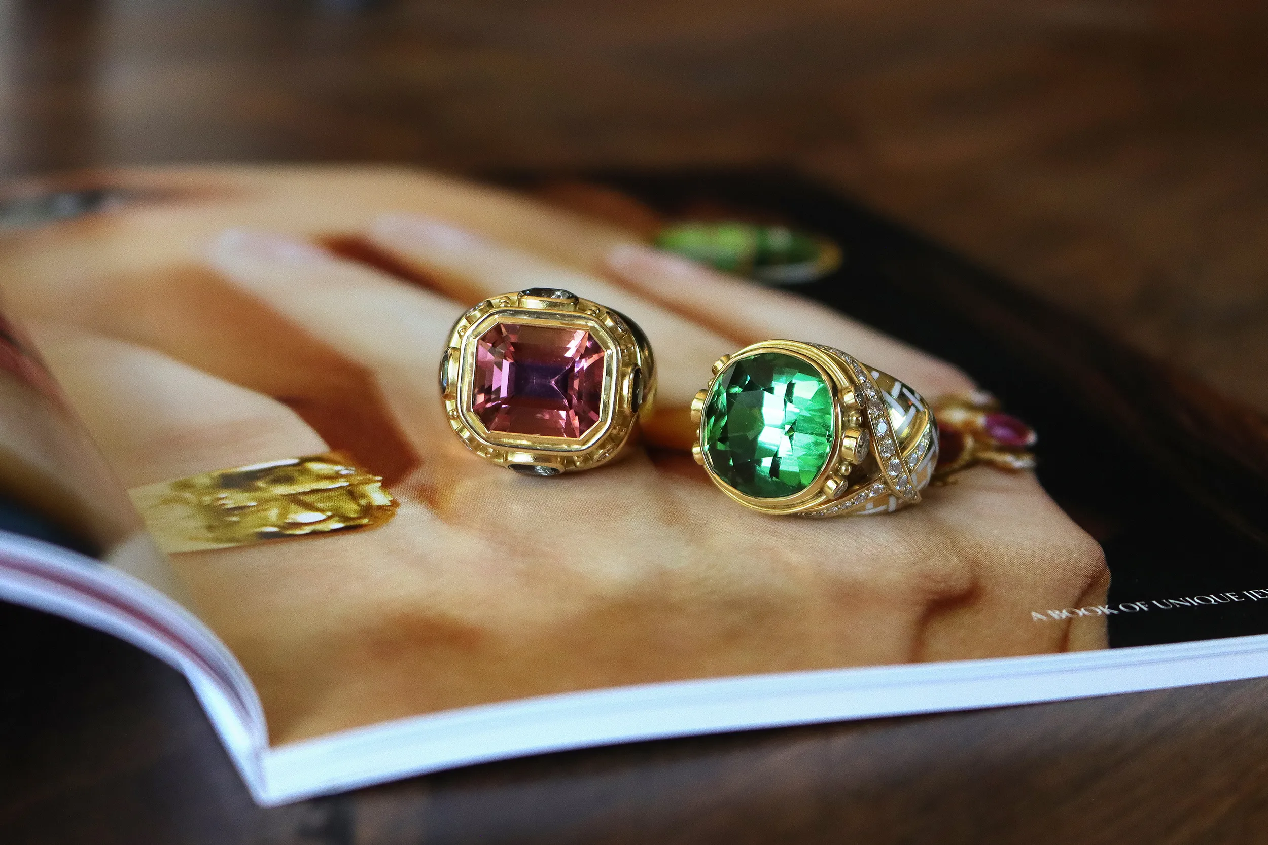 <p>Elizabeth Gage Charlemagne ring (left) with an octagon-shaped faceted pink tourmaline of 10.96 carats, four cushion-shaped faceted grey spinels totalling 2.24 carats, and brilliant-cut diamonds, alongside an 18.52 carat green tourmaline ring with a pavé-set asymmetric diamond collar and white enamel in a trellis pattern, both in 18k yellow gold</p>