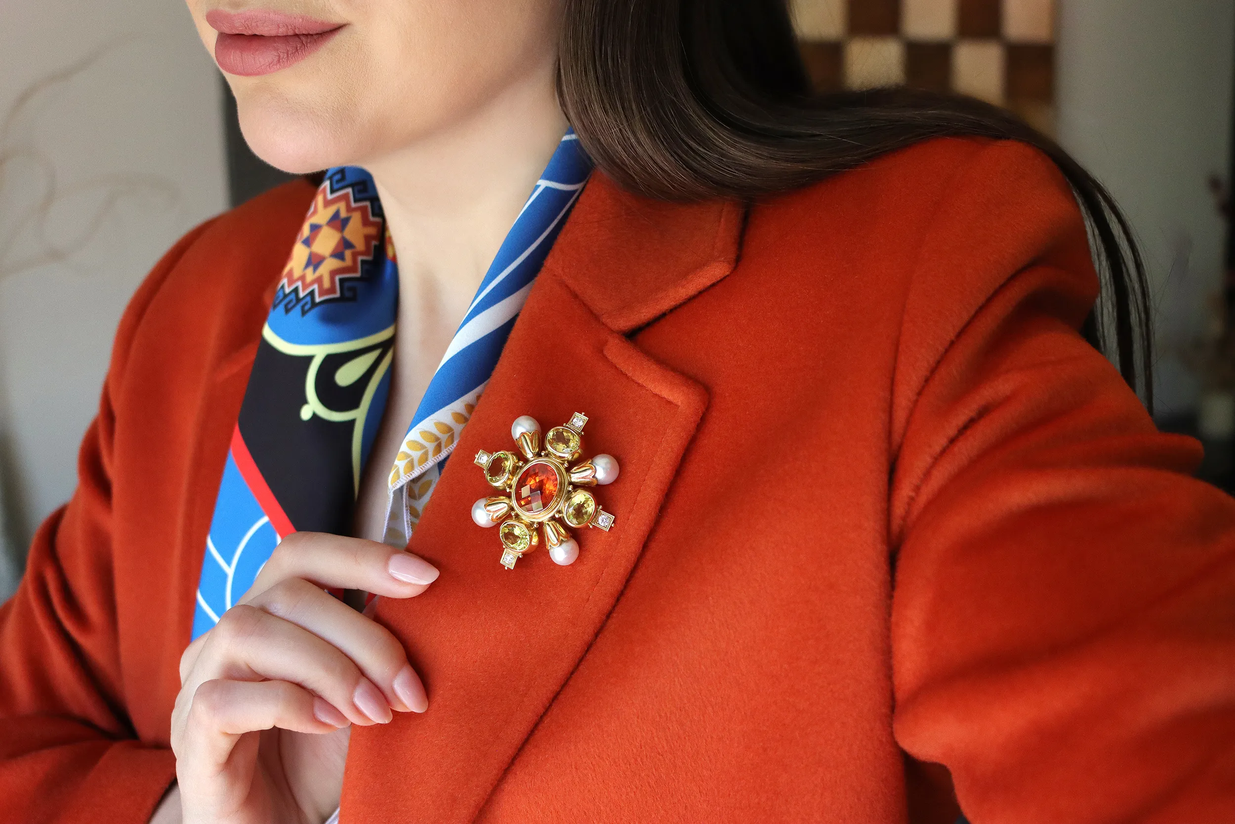 <p>Katerina Perezs wears an Elizabeth Gage Kiss pin with a chequerboard-cut oval-shaped mandarin garnet of 13.94 carats, four faceted oval-shaped yellow beryls of 9.16 carats, round brilliant-cut diamonds, natural grey cultured pearls and orange enamel in 18k yellow gold</p>