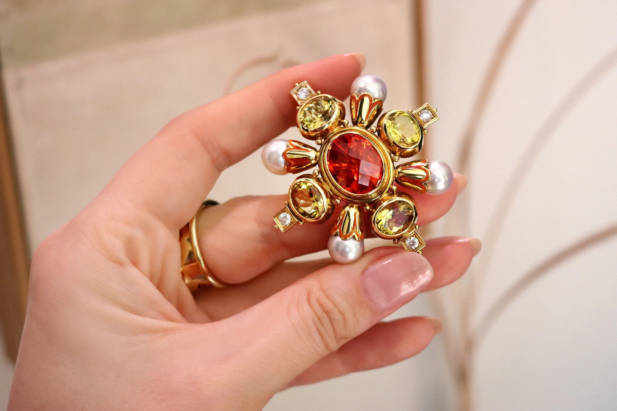 <p>A closer look at an Elizabeth Gage Kiss pin with a chequerboard-cut oval-shaped mandarin garnet of 13.94 carats, four faceted oval-shaped yellow beryls of 9.16 carats, round brilliant-cut diamonds, natural grey cultured pearls and orange enamel in 18k yellow gold</p>