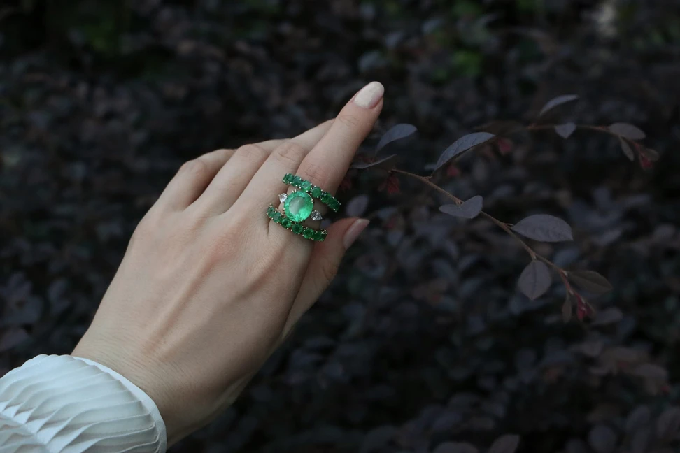 <p>Katerina Perez wears an oval-shaped emerald trilogy ring by Valentina Fine Jewellery alongside two round brilliant-cut emerald eternity rings </p>