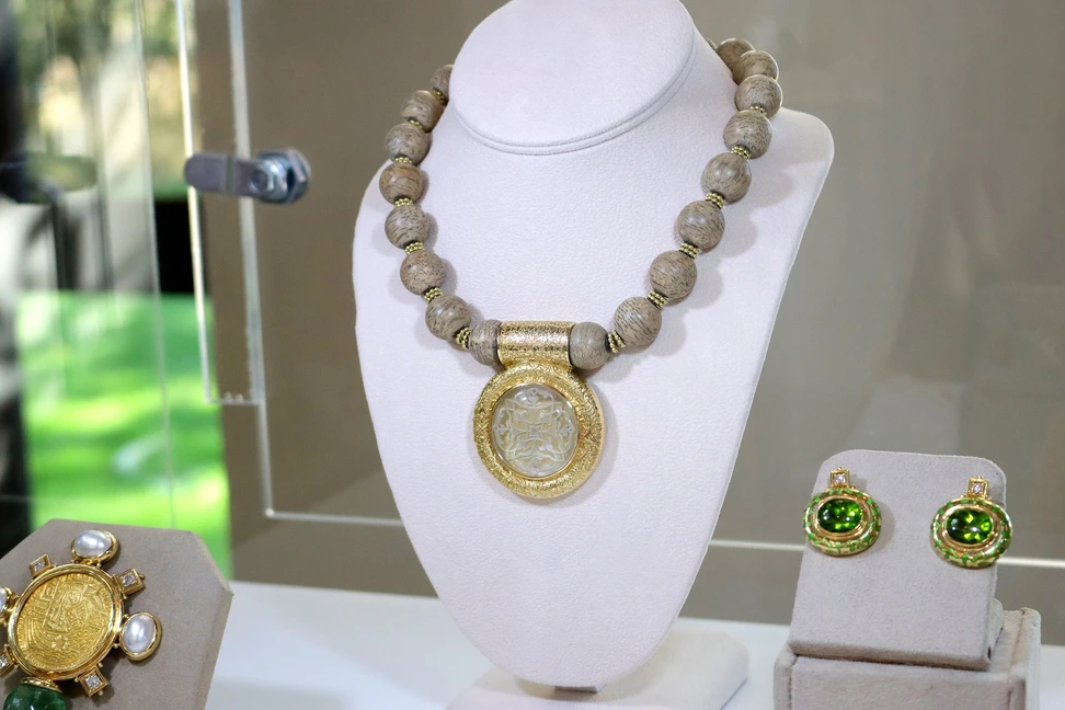 <p>The Elizabeth Gage Grafiko Jasper necklace, set with 20 pieces of Grafiko jasper and a 49.58 carat rock crystal cabochon engraved intaglio with a Celtic design, shown here alongside the King Edward IV Gold Royal Coin pin (left) with an antique coin, mabé pearls, diamonds and fluorite, and the Persian Queen earrings with 15.67 carats of oval-shaped peridot, green enamel and brilliant-cut diamonds, all in 18k yellow gold</p>