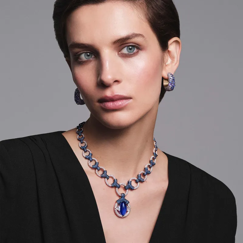 A model wears Pomellato Stile Libero Eye of Tanzanite necklace in rose gold with 1 cabochon marquise-cut tanzanite, 2 trillion-cut diamonds, 1,320 sapphires and 1,951 diamonds and Serti Libre earrings in rose gold with 26 pear-cut purple sapphires, 208 purple sapphires and 208 tanzanites