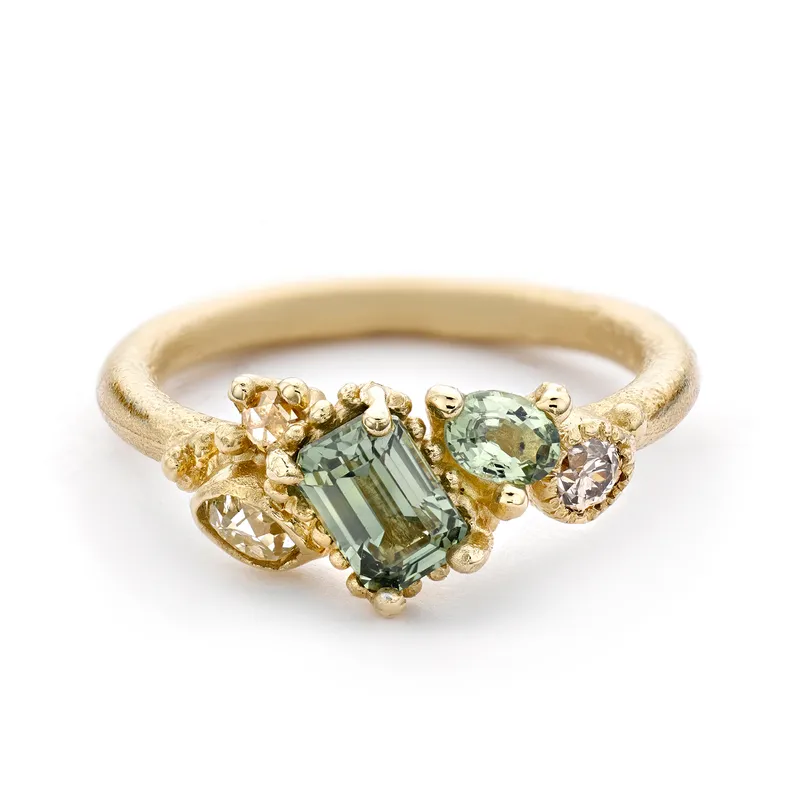 <p>Asymmetric Cluster ring in yellow gold, set with emerald-cut green sapphires</p>
