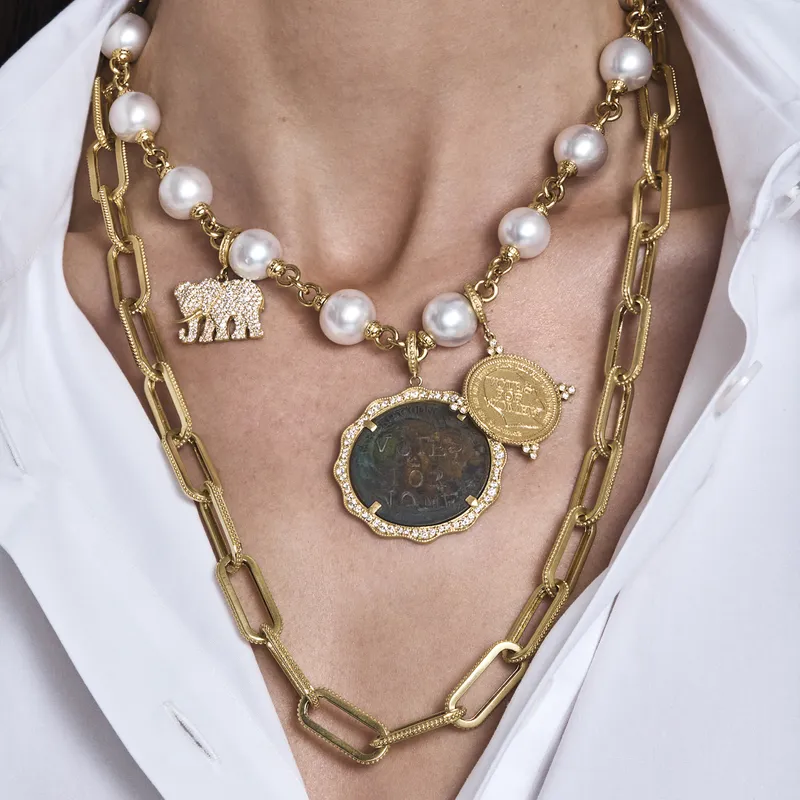 <p>A model wears a Vintage Suffragette Coin pendant with a scalloped diamond bezel alongside the Suffragette Coin charm with diamonds, both from the Empowerment collection</p>