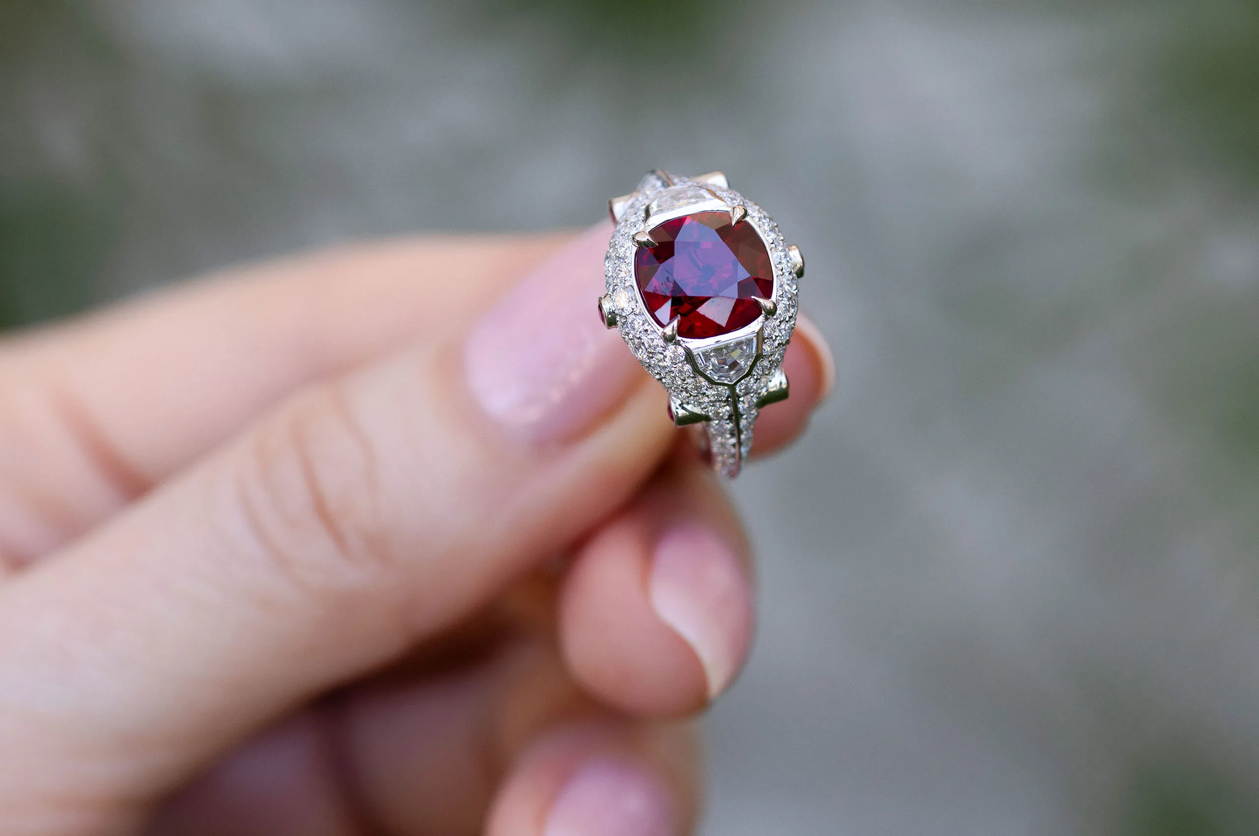 The cushion-cut ruby sits high within the diamond-set platinum mount, with epaulette diamonds visible on either side