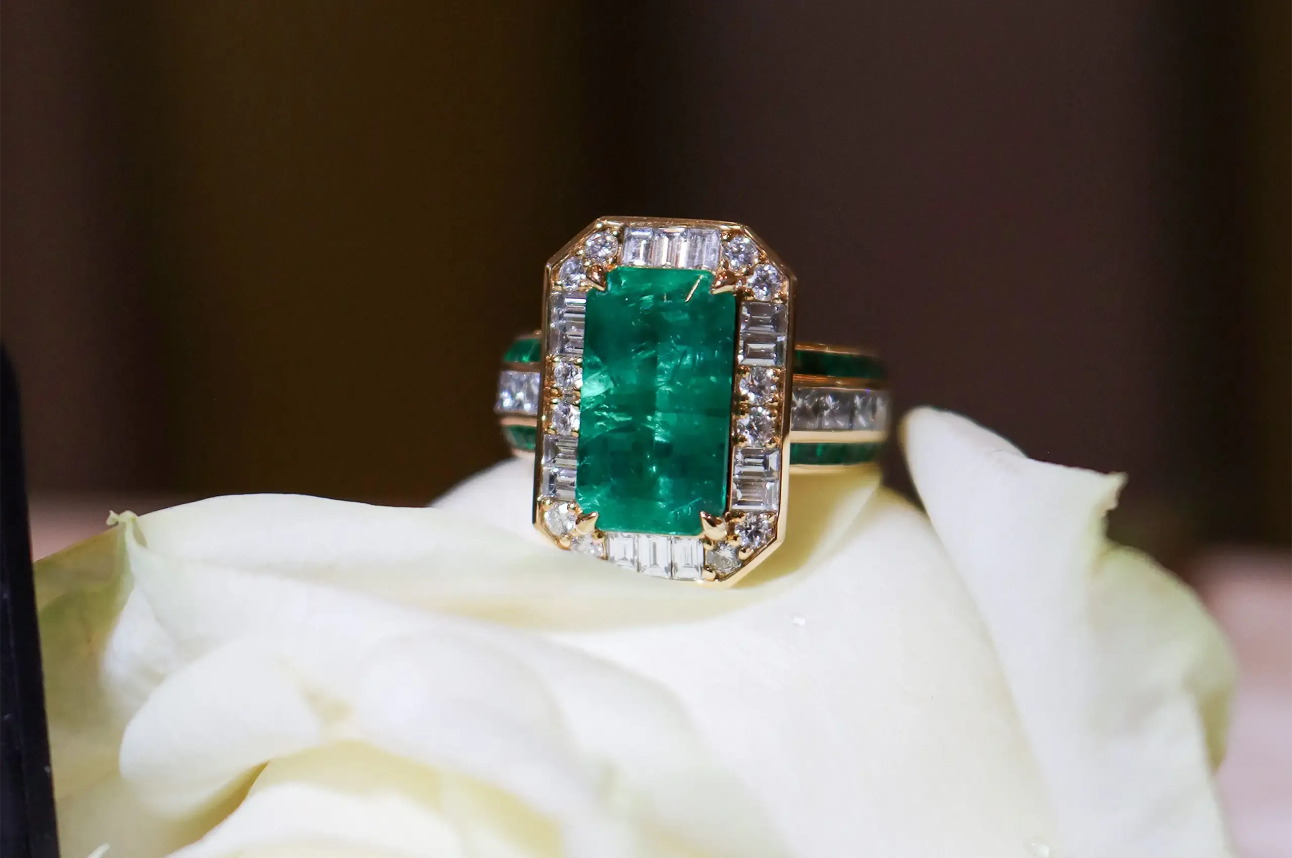 An emerald cocktail ring by ANTON Jewellery, surrounded by a geometric arrangement of baguette-cut diamonds