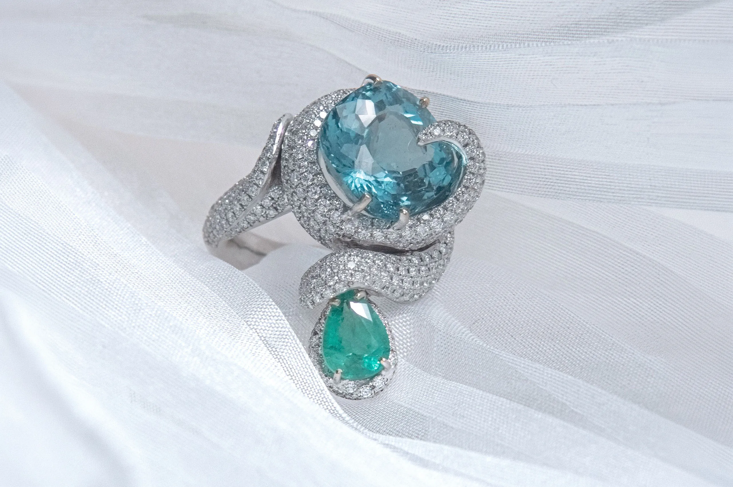 A d'Avossa ring with a cushion-cut apatite and a pear-shaped emerald, joined by a wave of diamonds