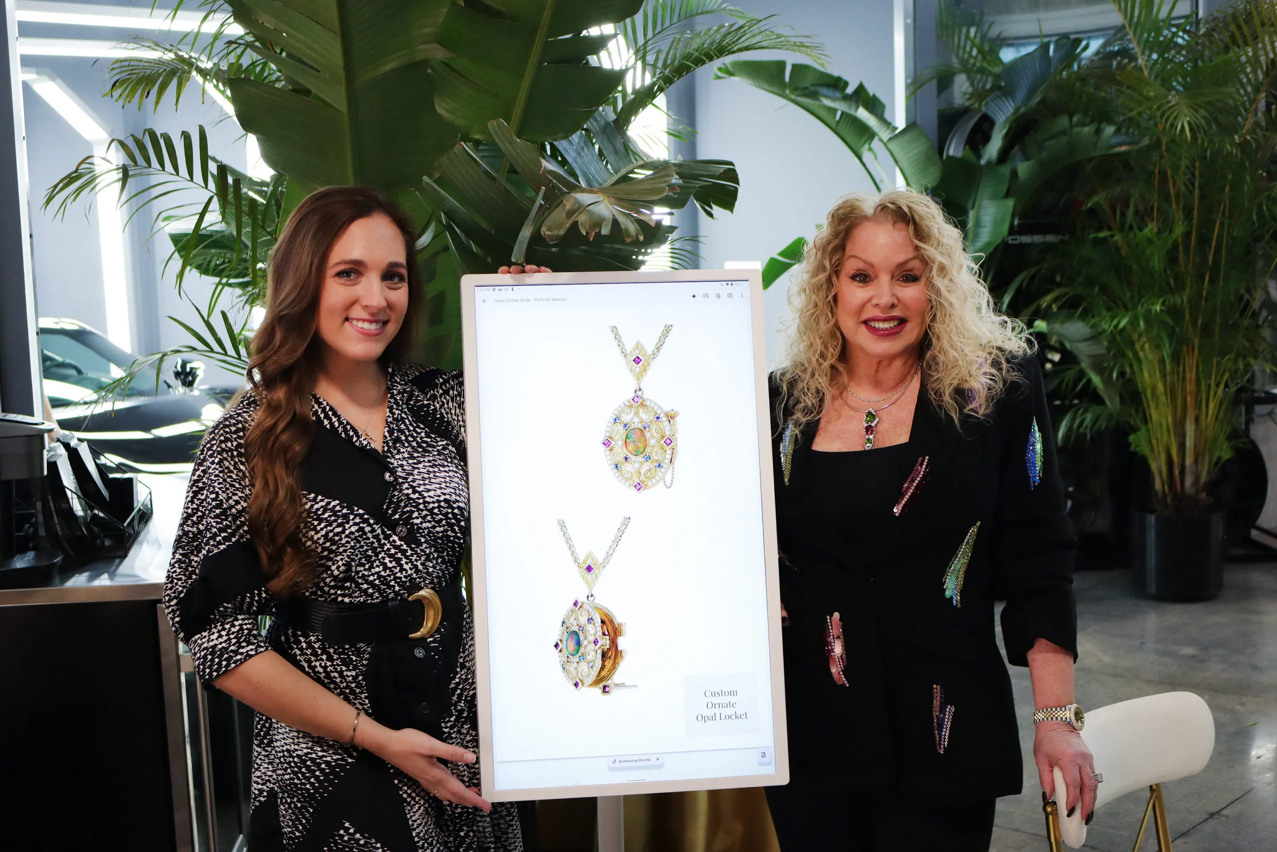 <p>Nicole Leiner and Robin Callahan of Palm Beach Gems by Nicole with a digital screen spotlighting a detailed custom-made opal locket</p>