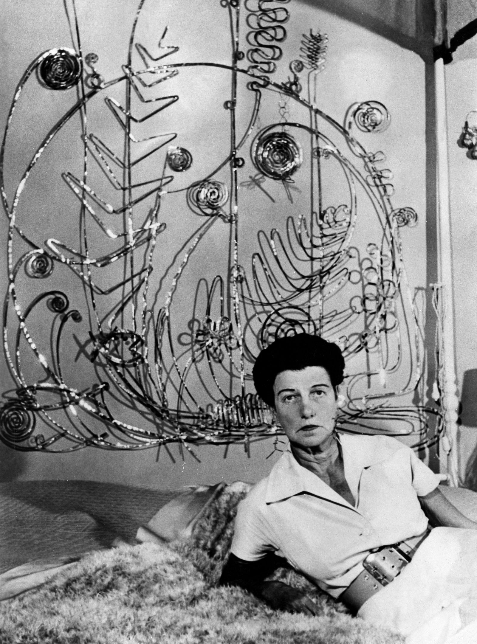 Peggy Guggenheim wearing Alexander Calder earrings beneath one of his sculptures, reflecting her role as both collector and champion of artist made jewellery.