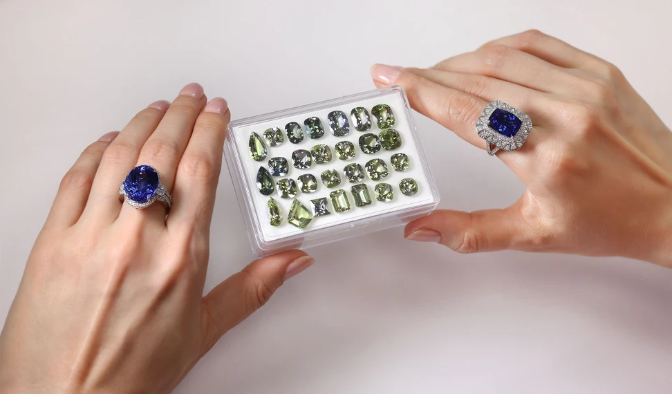 <p>Katerina Perez wears a pair of tanzanite dress rings while examining a selection of green zoisite gemstones from the Royal Touch Group</p>

