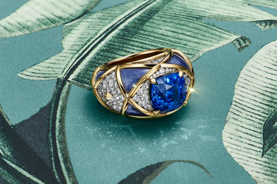 A lattice of gold, lavender paillonné enamel and diamonds evokes the patterned surface of a pineapple in this Tiffany & Co. Blue Book ring, set with a 7.76-carat unenhanced cushion-cut sapphire