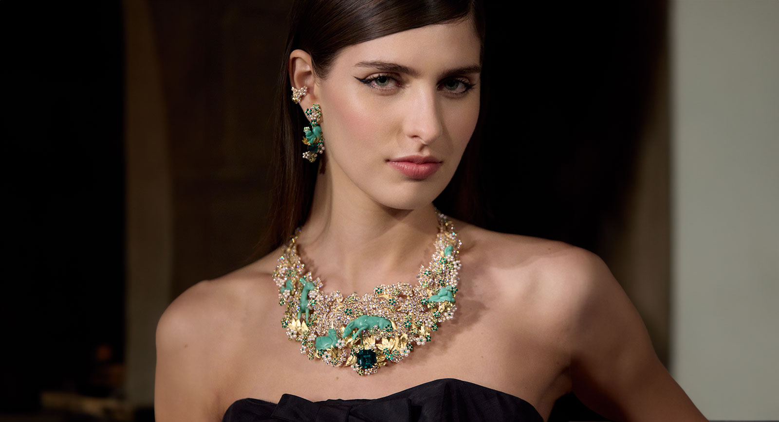 A model wears the Diorama Foret Enchantée necklace from the Diorama & Diorigami High Jewellery collection, set with a 16.16 carat Colombian emerald, further emeralds, tsavorite garnets, diamonds and pearls with glyptic chrysoprase animals in three-dimensional form, all in engraved 18k yellow gold 