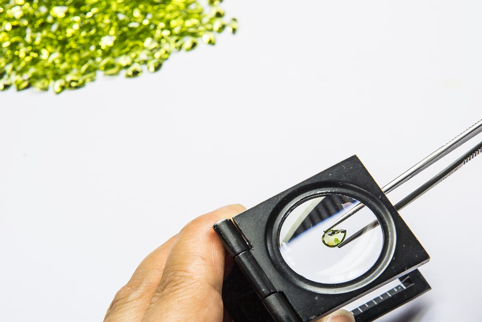 A faceted Fuli Gemstones peridot is examined beneath a magnifying glass