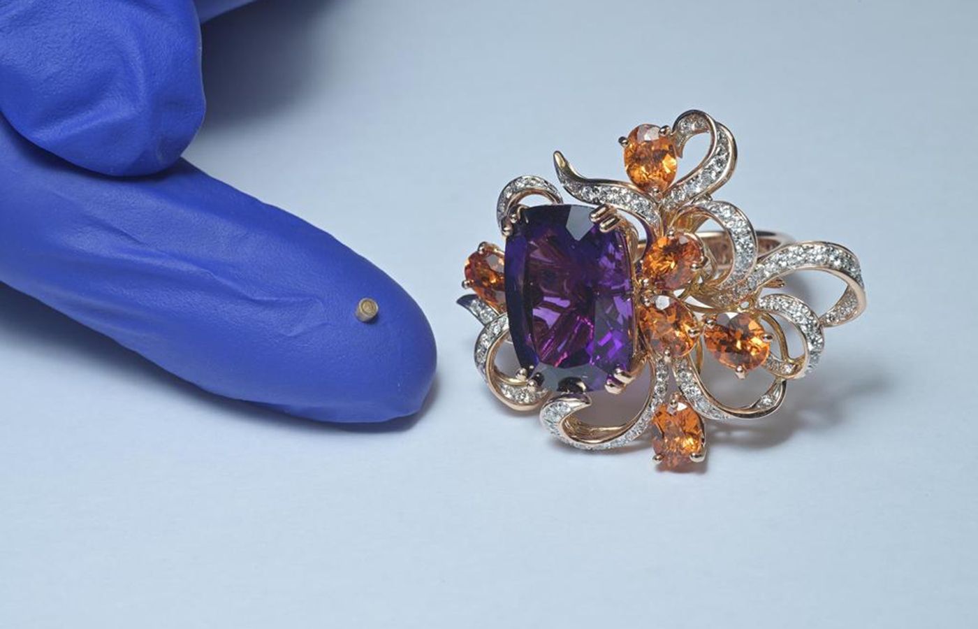An example of a tiny Caratell RFID micro-chip invented by Michael Koh alongside a ring with Mandarin garnets