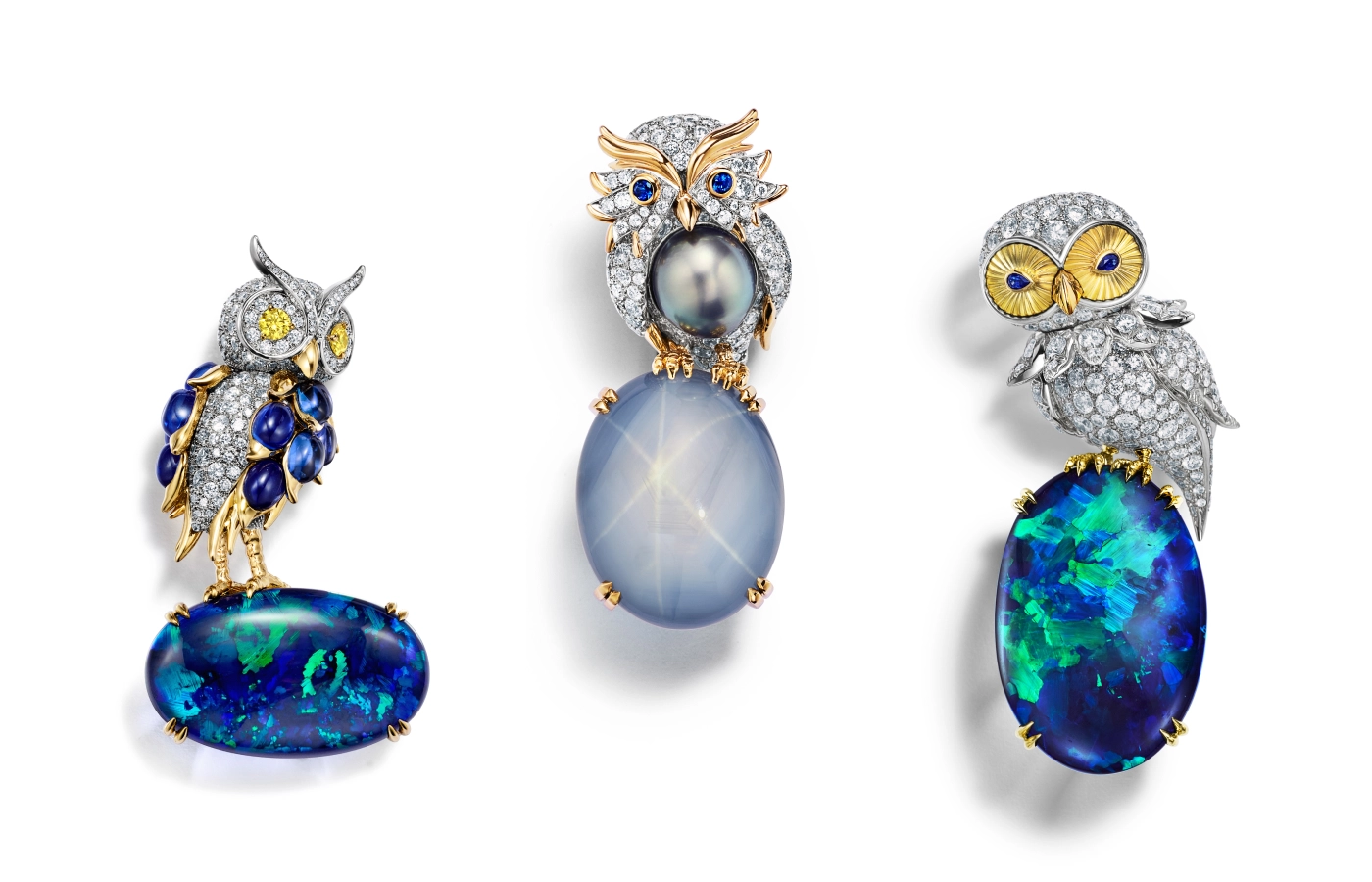 A trio of Tiffany Céleste 'Owl on a Rock' brooches from the Blue Book 2024, perched on oval black opals and a star sapphire 