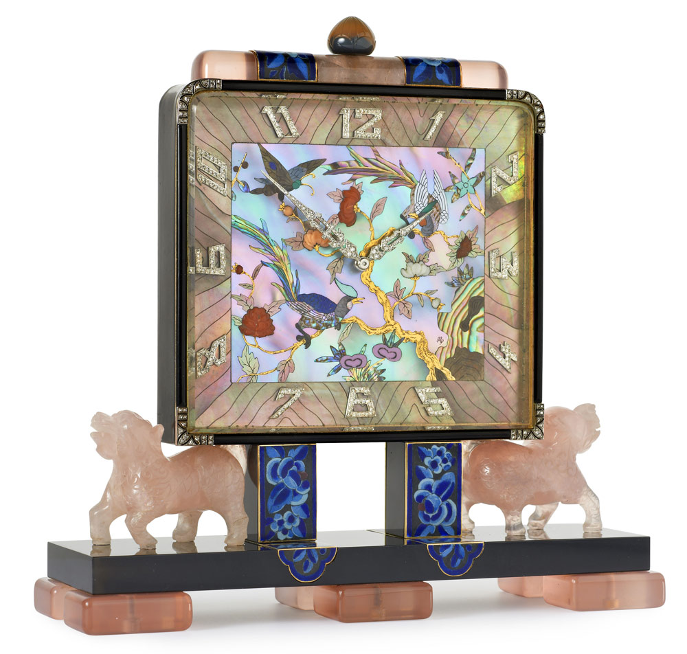 Exquisite Art Deco Chinoiserie desk clock with a rectangular dial of mother-of-pearl with floral and bird decoration enhanced by carved coral, applied rose-cut diamond Arabic chapters and pavé-set diamond hands. Black laquer case with rose quartz surmount, a carved agate crown and blue enamel floral panels, all on carved rose quartz dogs and blue enamel floral pillars. The black laquer base has six rose quartz feet and case contains a mechanical movement. By Lacloche Freres, Paris c1925 with dial decoration by Vladimir Makovsky
